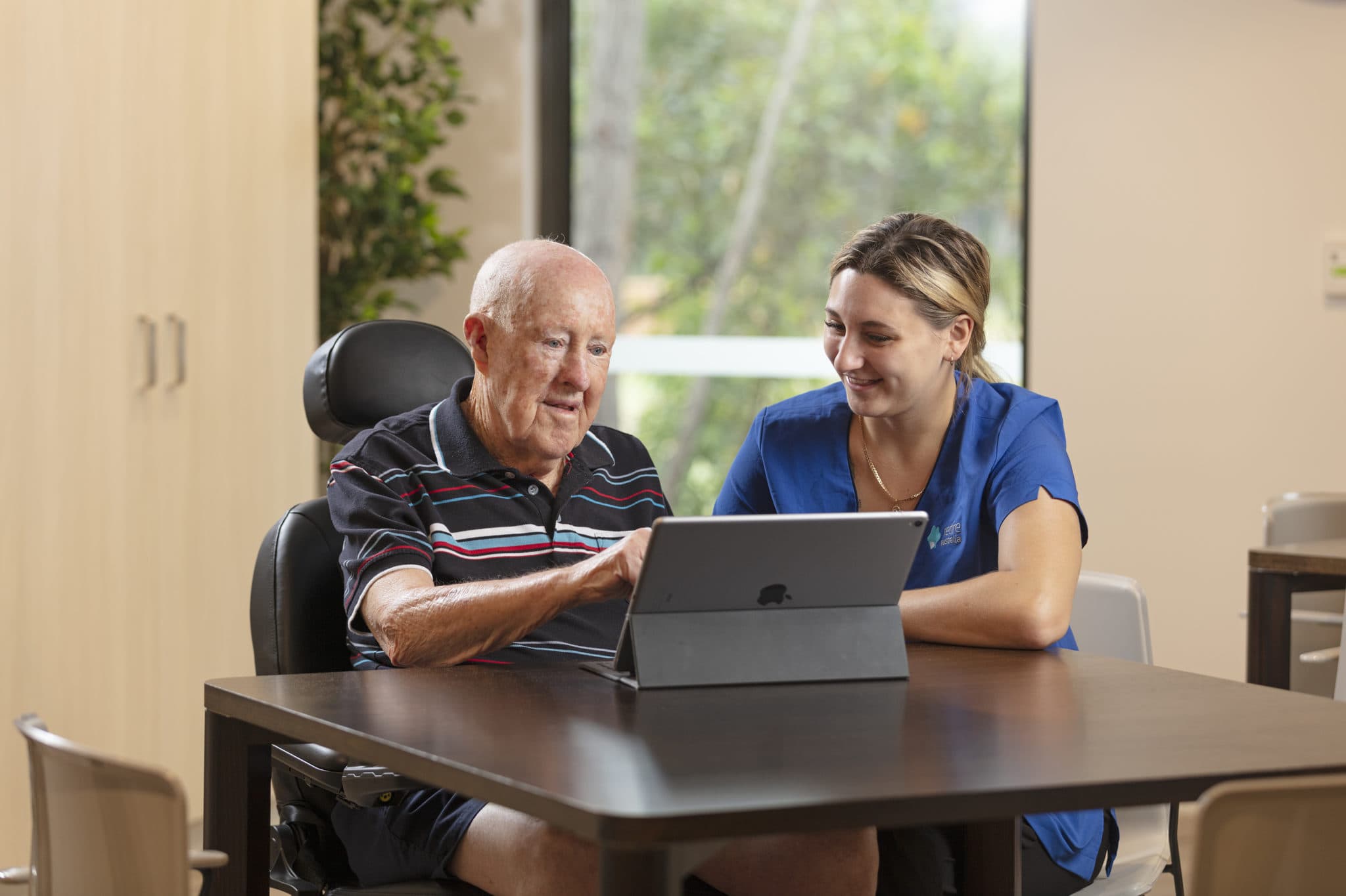 Staff member assisting elderly man with tablet