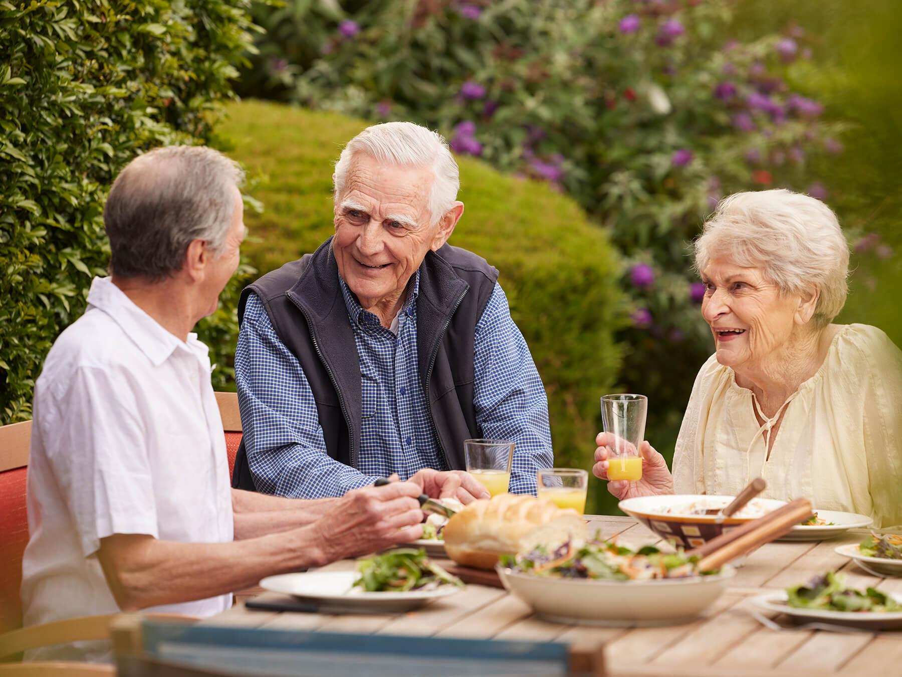 Three residents smiling and talking over their lunch outside