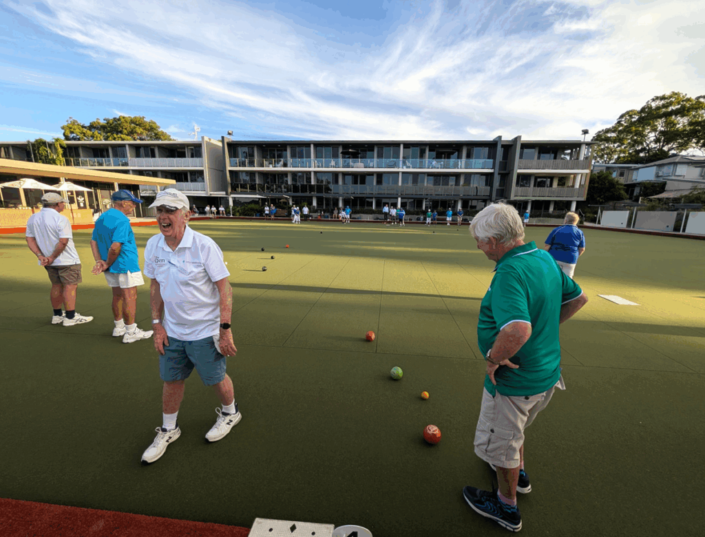 Three bowlers playing bowls. Man in a white shirt and cap smiling